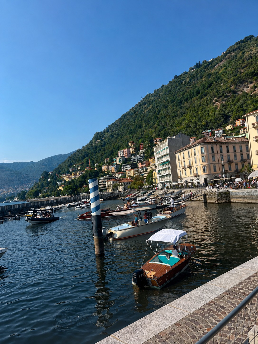 Boats moored in a Lake Como harbor below a colorful hillside town.