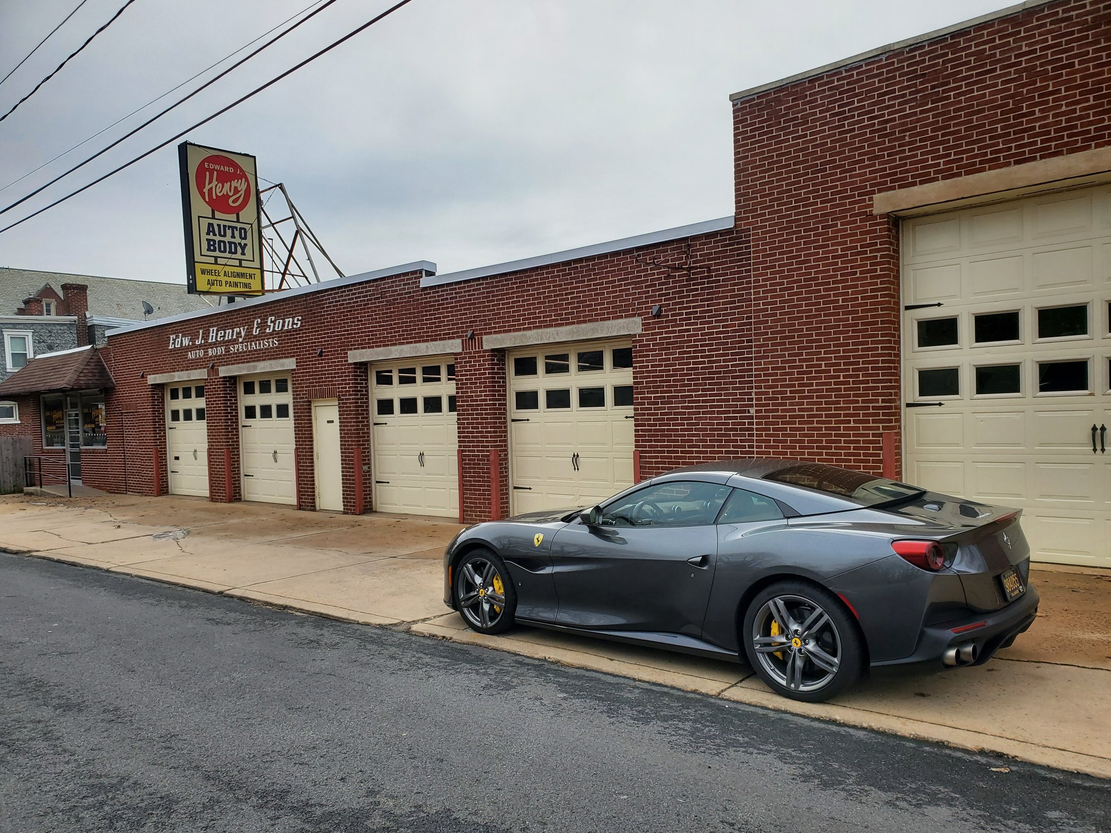 The vintage Henry Auto Body sign above the red brick storefront on West Fourth Street in Wilmington, a gray Ferrari Portofino at the curb