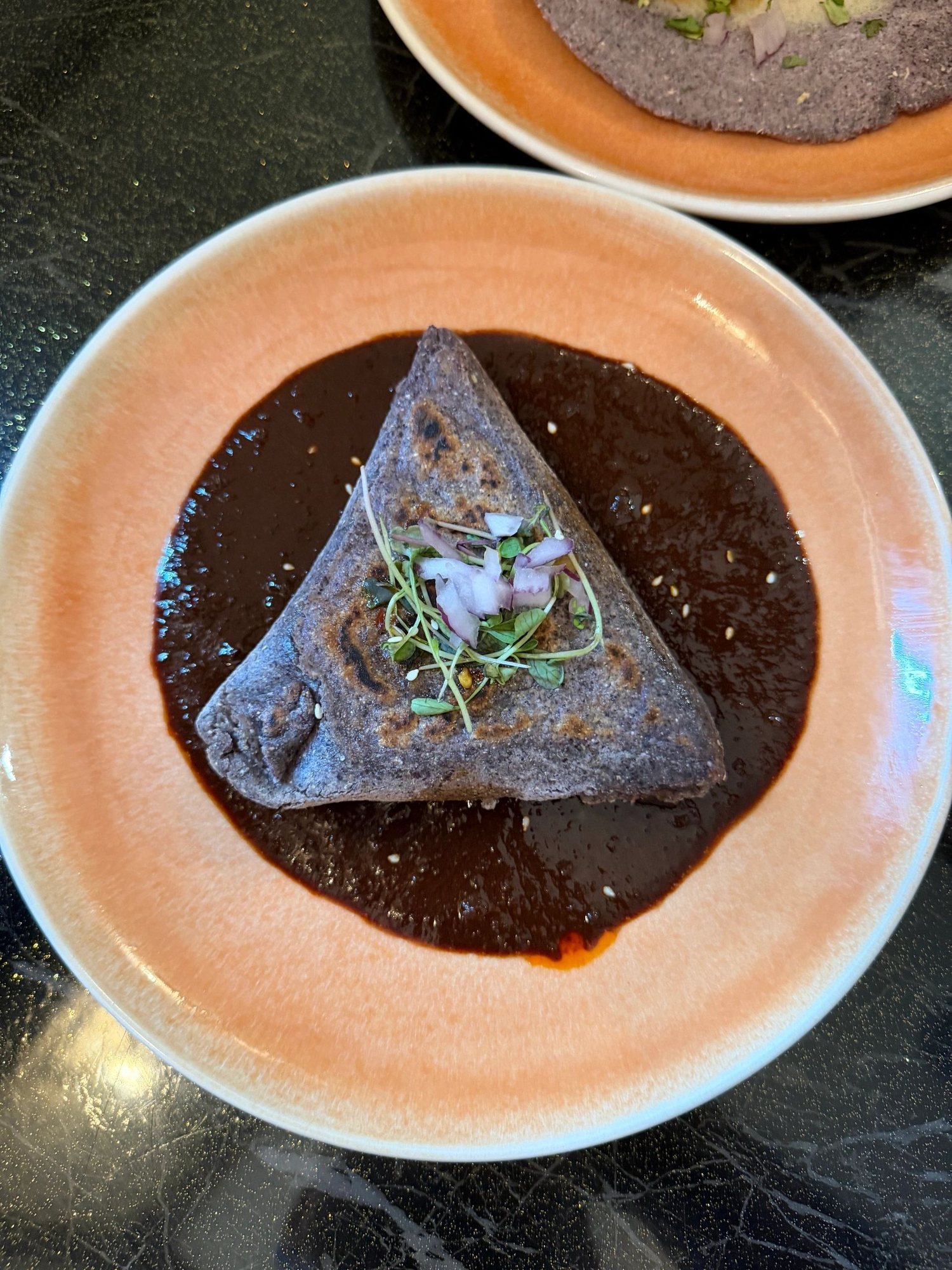 A triangular blue-corn preparation set in dark mole on a coral plate at MAIZ.