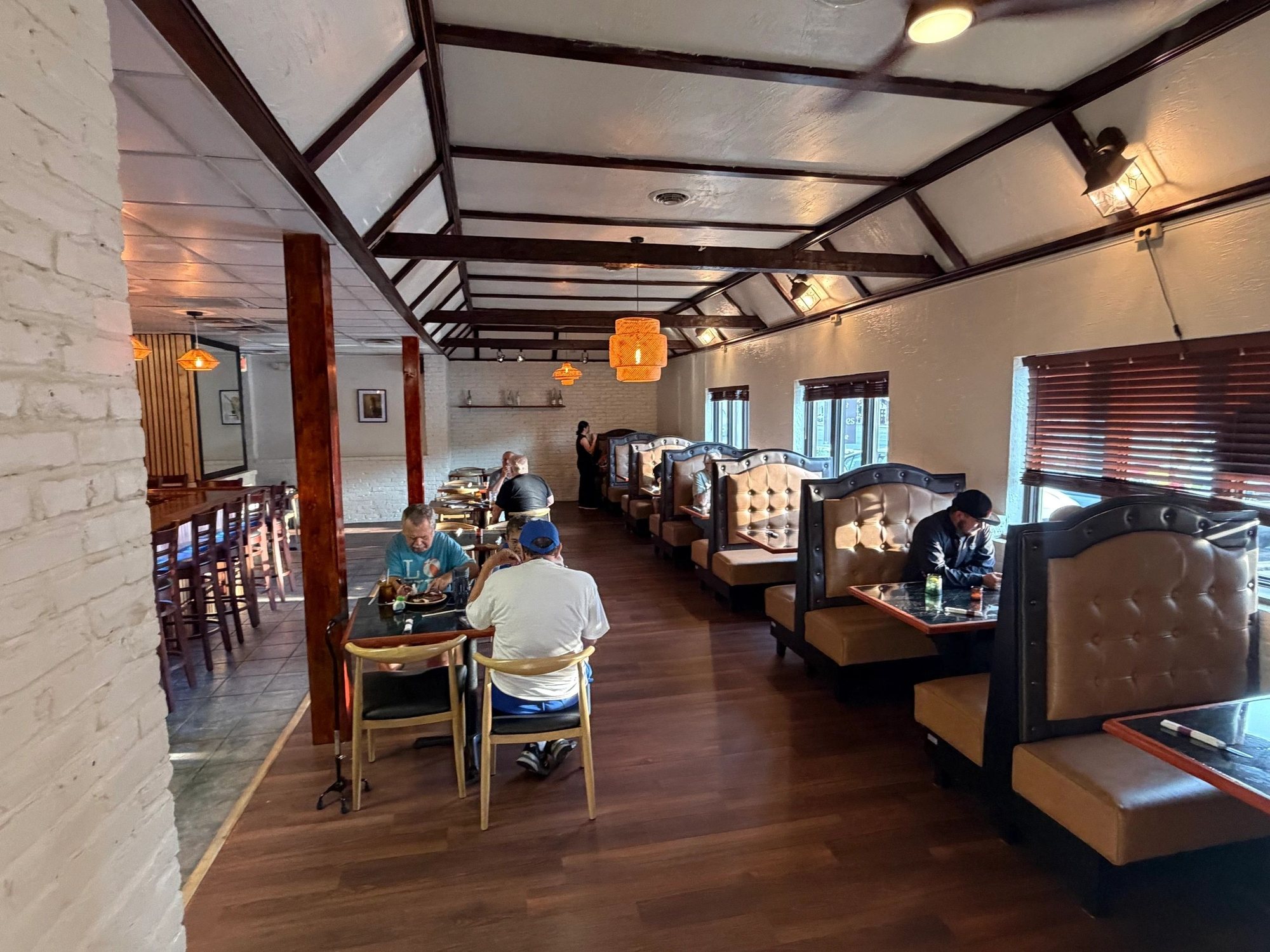 The long banquette row inside MAIZ in Wilmington, with white brick walls, wood beams and woven pendant lights.